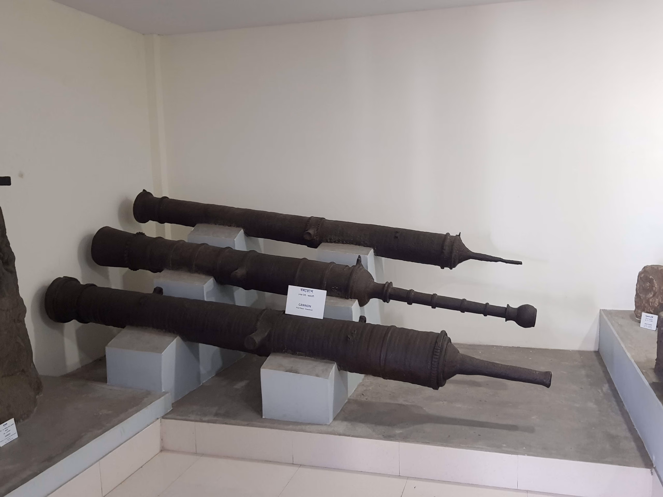 Three large cast-iron cannon of the Ahom period displayed on plinths in a museum