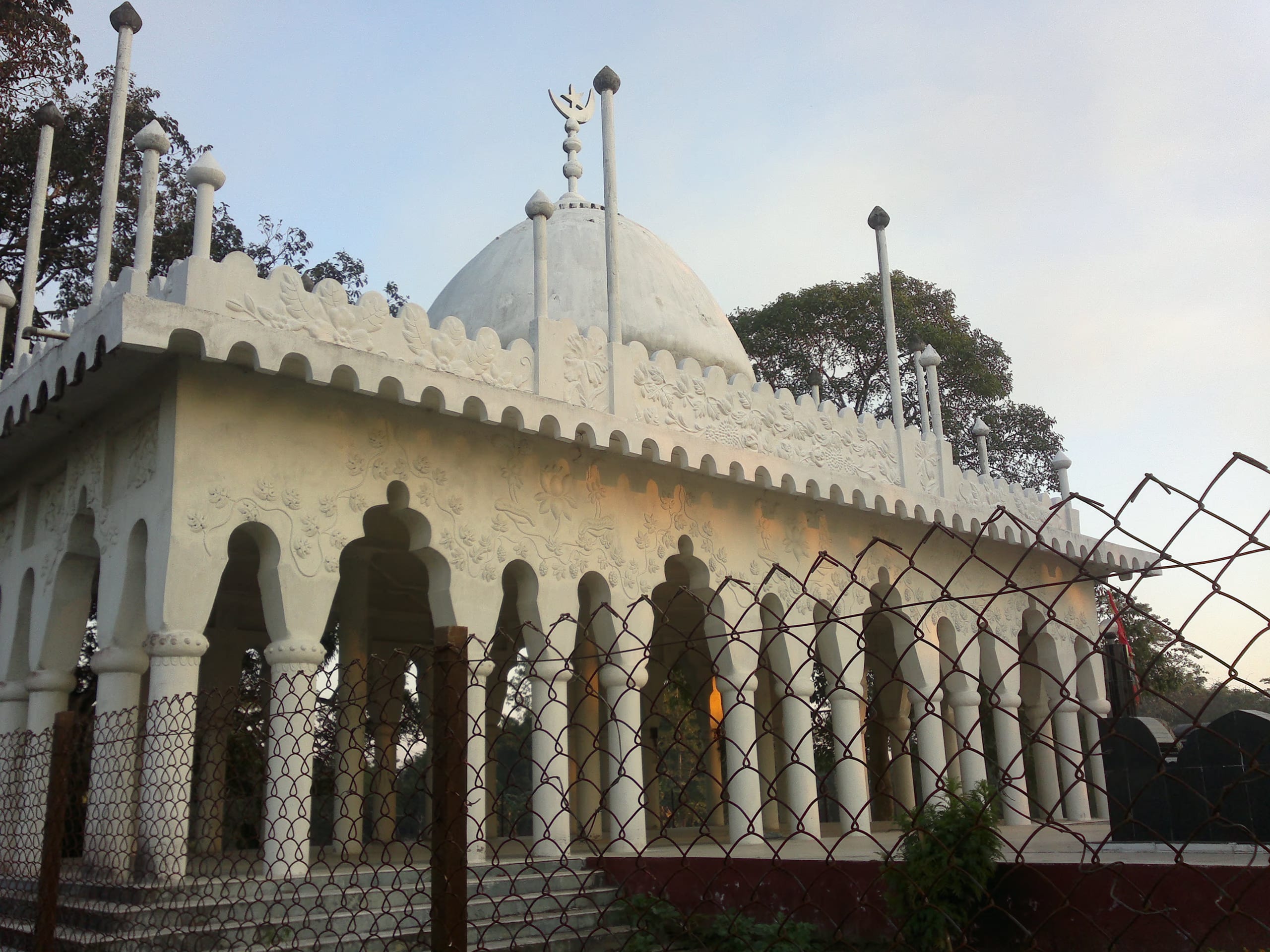 White domed shrine of Ajan Pir with floral-relief plasterwork and an arcaded verandah on the river island at Saraguri Chapori