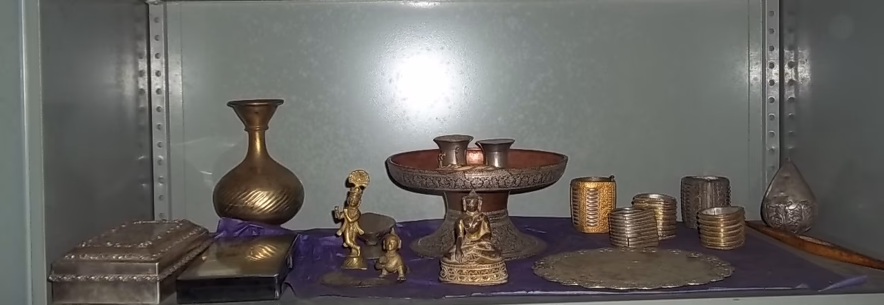 A shelf of gold and silver objects — a gilt Krishna figure, an ornate offering stand, silver caskets and bangles — at Bengenaati Sattra