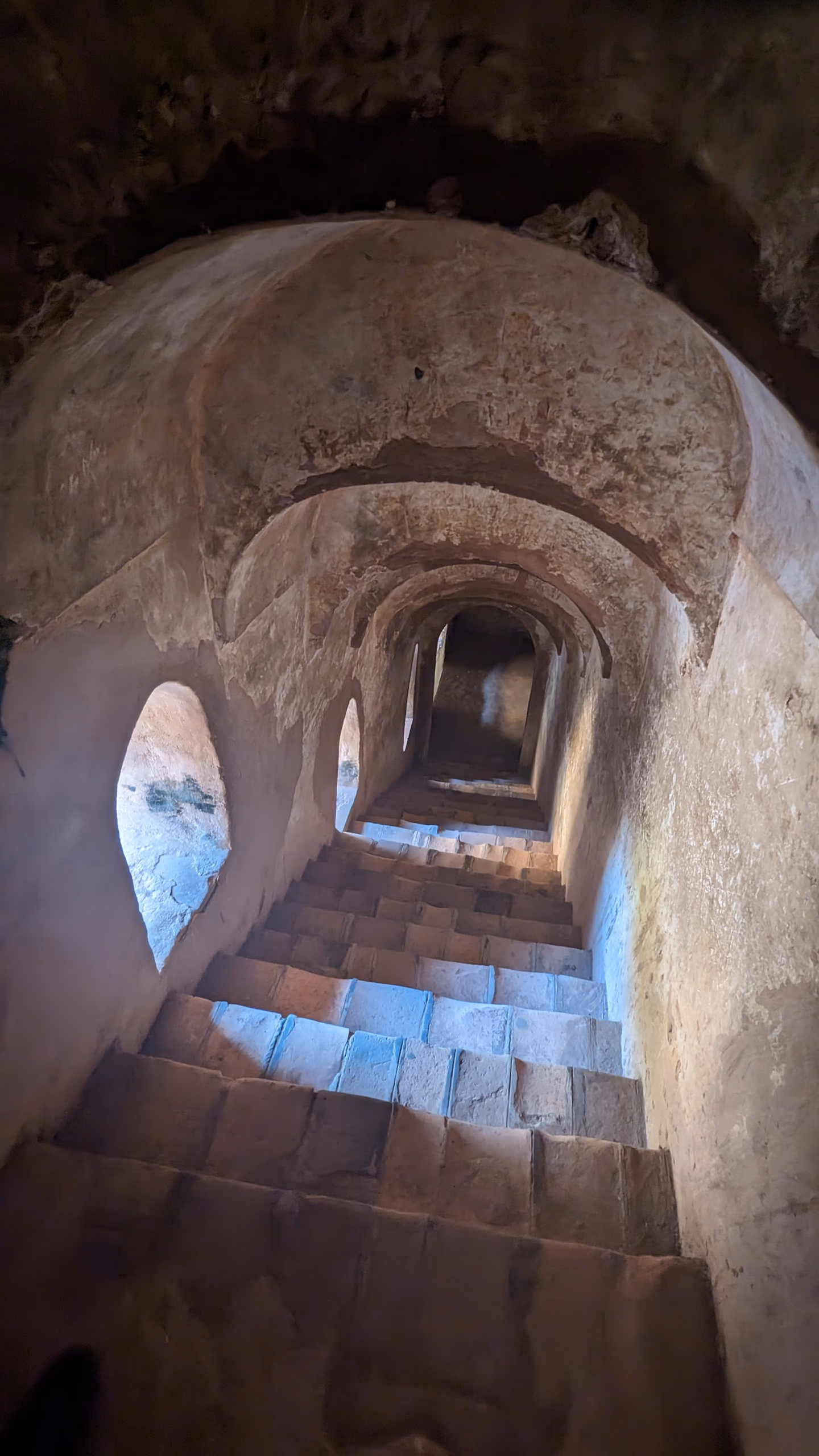 A vaulted brick staircase descending into the lower storeys of the Talatal Ghar, daylight falling from a side opening onto worn masonry steps