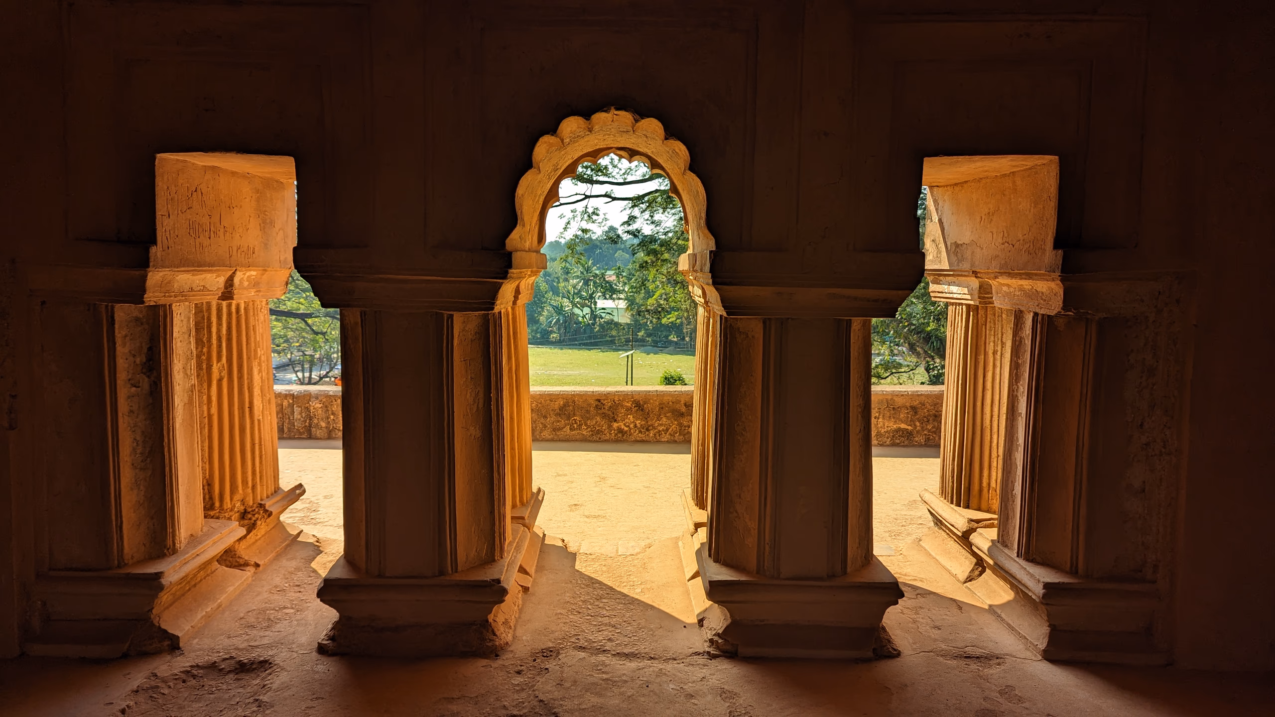 Cusped masonry archway inside the Kareng Ghar palace at Garhgaon, opening onto green grounds