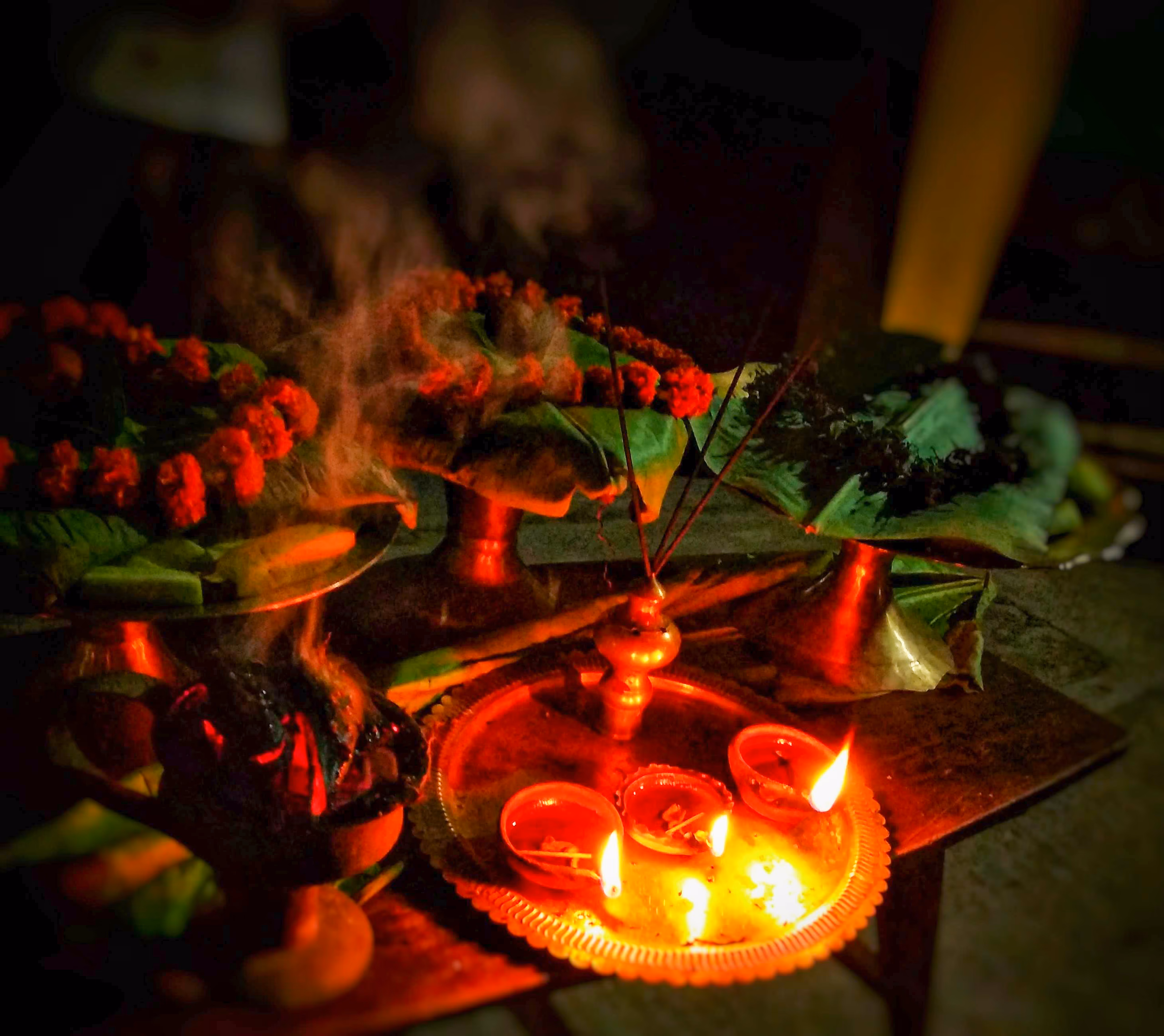A brass plate of lit oil lamps, marigolds on leaves, and burning incense, an offering during a festival celebration at Hajo