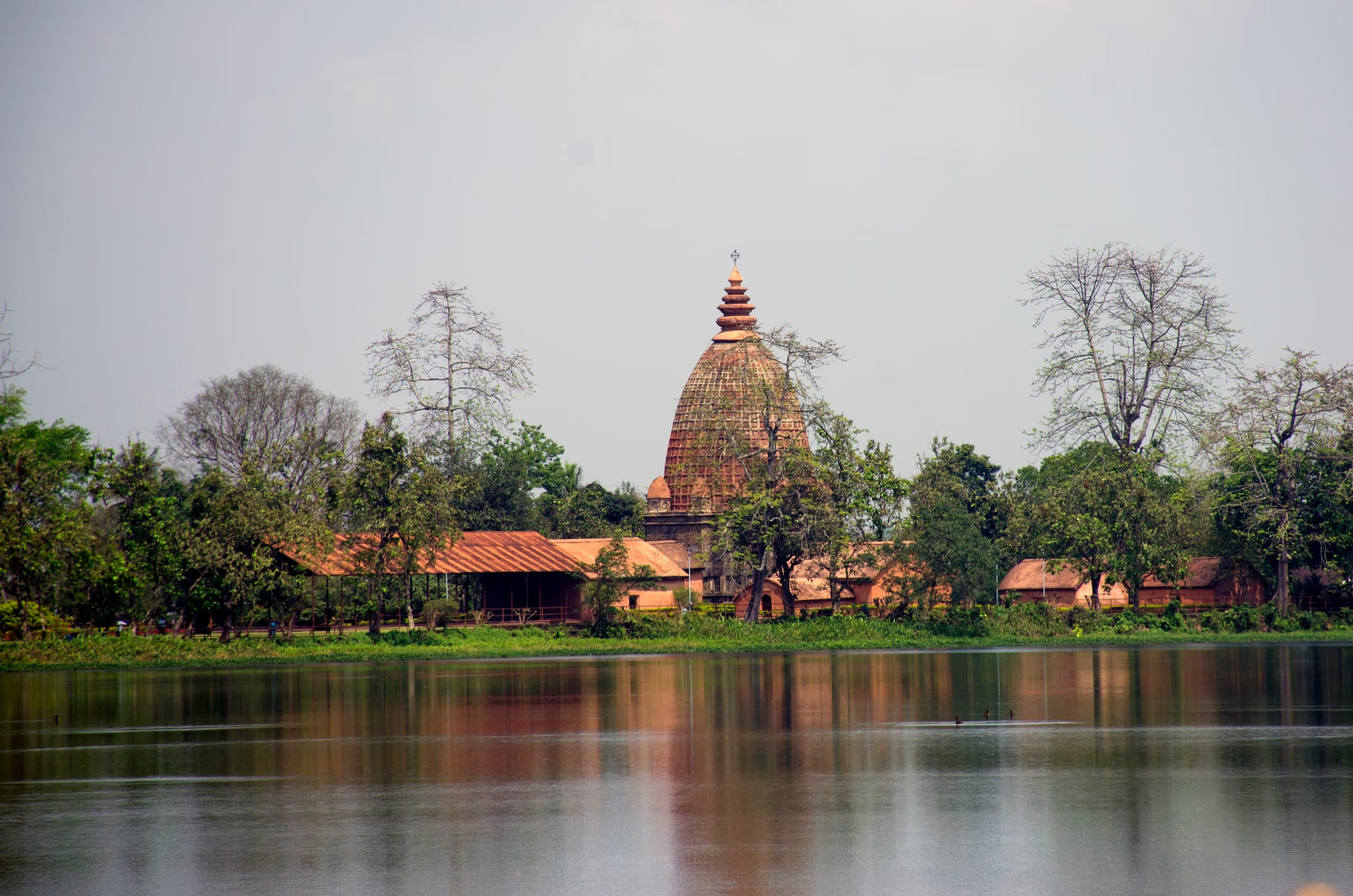 The Joysagar tank seen across the water to a bankside Ahom dol temple and a low pillared hall, reflected in the great sheet of water