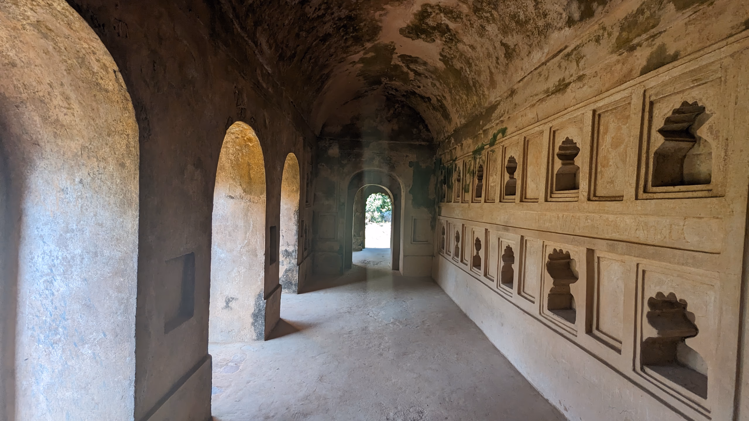 A vaulted brick corridor inside the Talatal Ghar, arched openings along one wall and carved plaster niches along the other