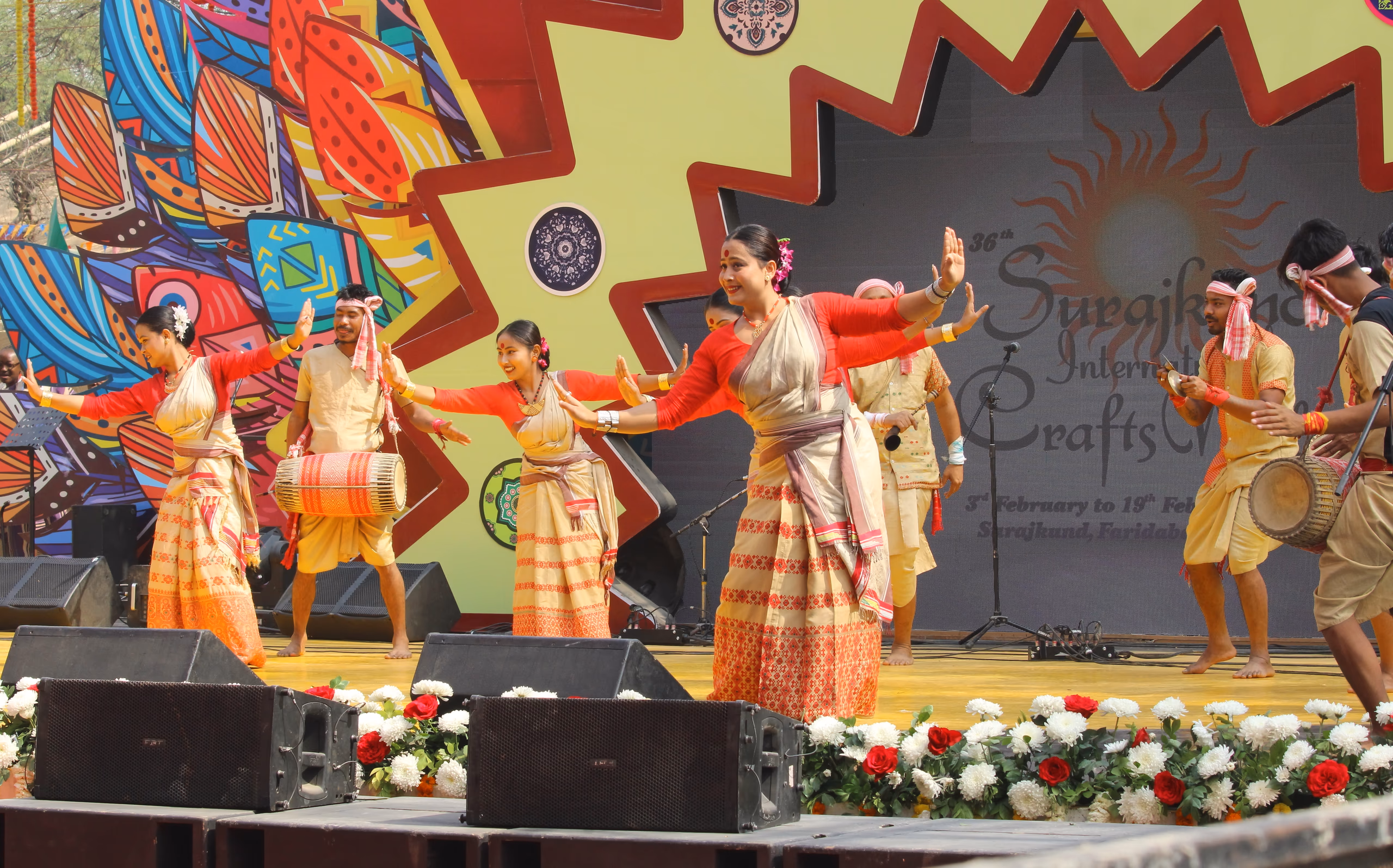 Bihu dancers performing on a stage, the women with a gamosa draped across the torso and the men wearing gamosa headbands while playing the dhol