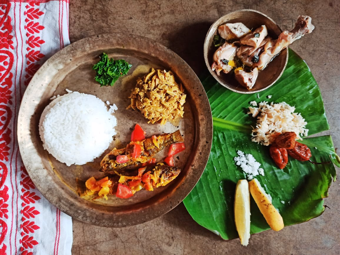 An Assamese lunch on a bell-metal plate with rice, fish, and condiments, beside a banana leaf