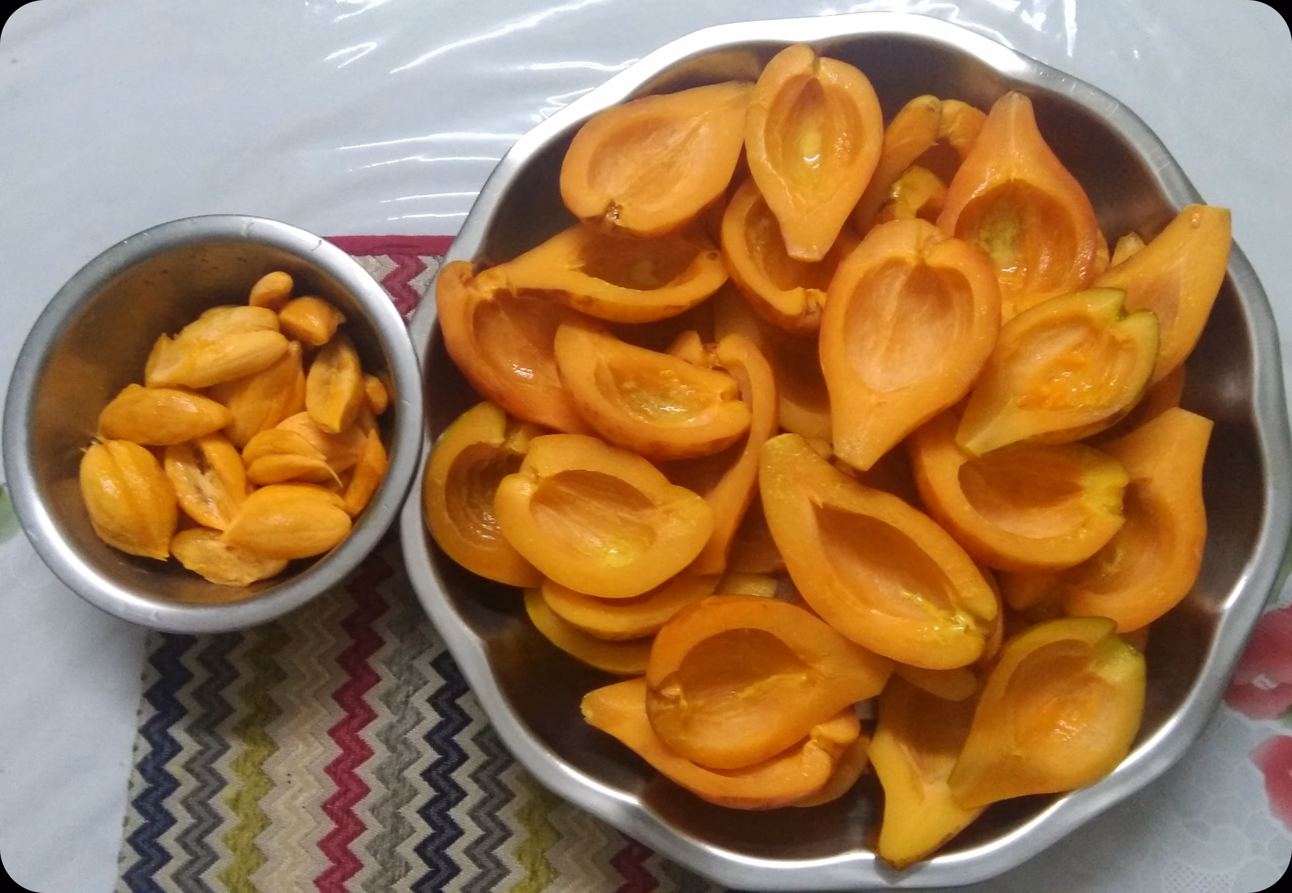Halved bright-orange thekera fruit arranged in a metal bowl with separated seeds in a smaller bowl