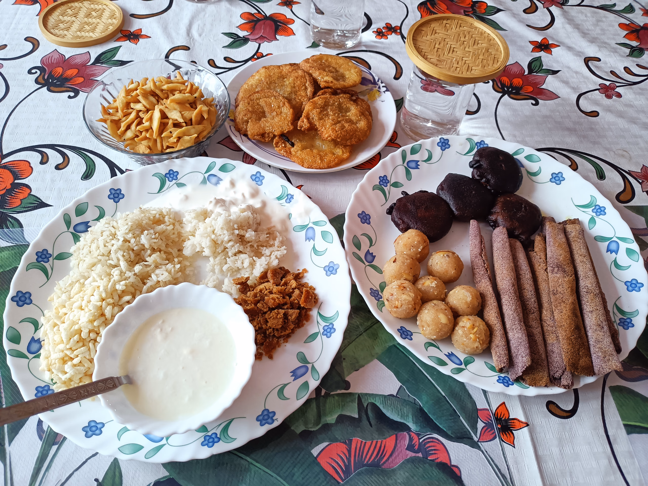 A Bihu spread of jolpan with curd, coconut laru balls, til pitha rolls and fried pithas on patterned plates